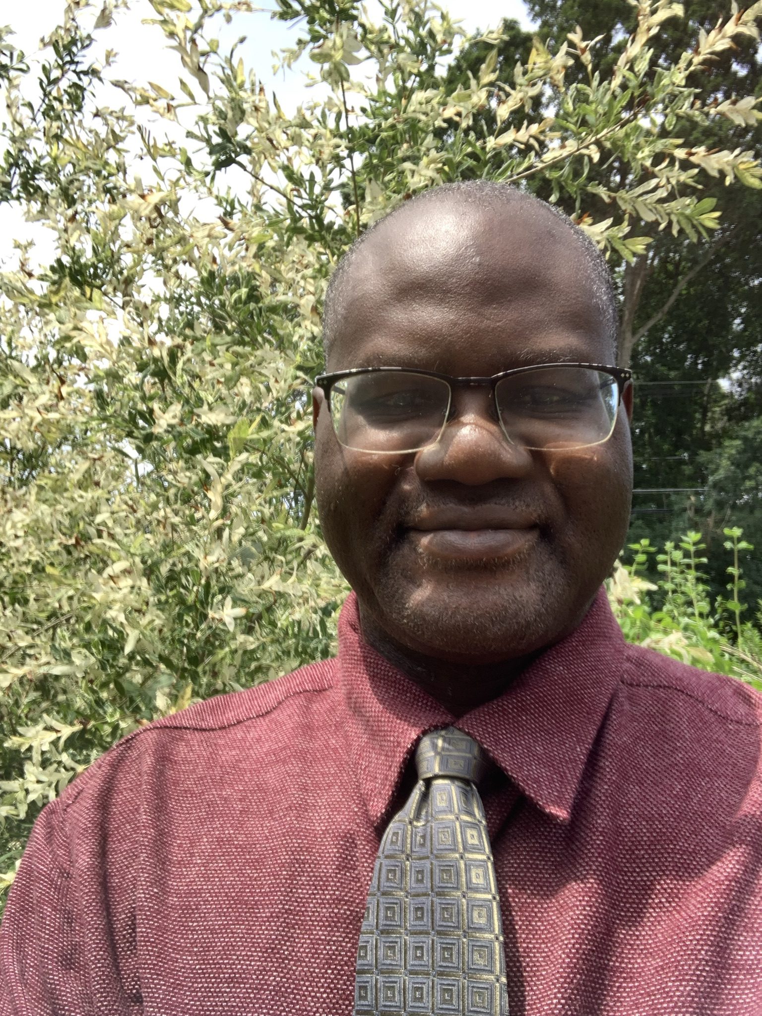 Man in a red shirt and green tie smiling.