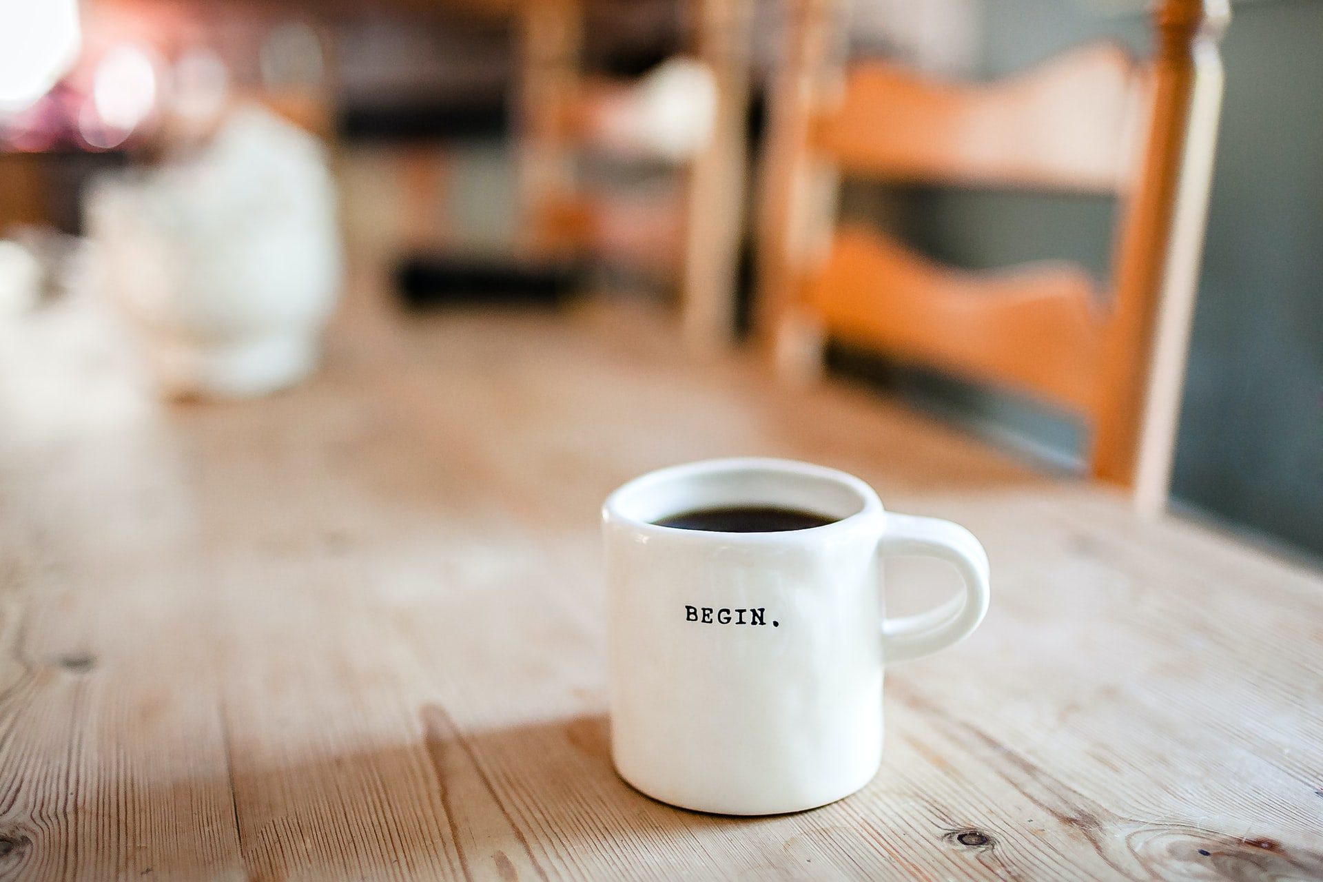 Coffee cup with the word "Begin", on it sitting on a wooden table.