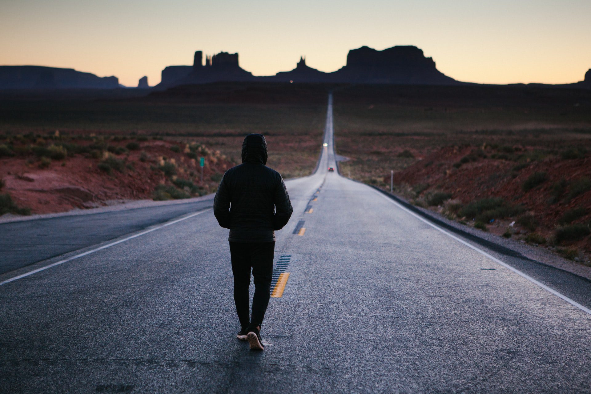 Man wearing black walking down a road in the desert.